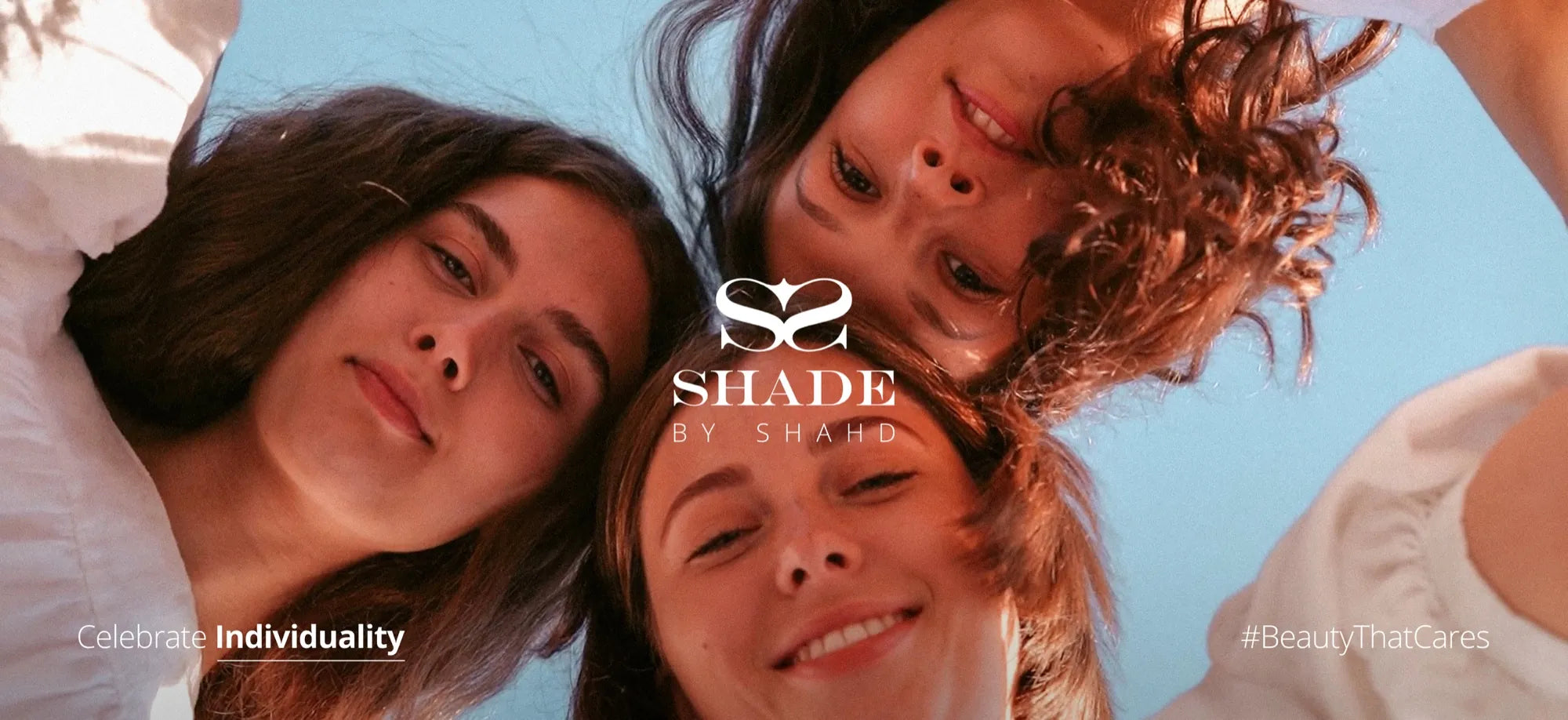 Three women looking down at the camera under a blue sky, with the Shade by Shahd logo and the line Celebrate Individuality